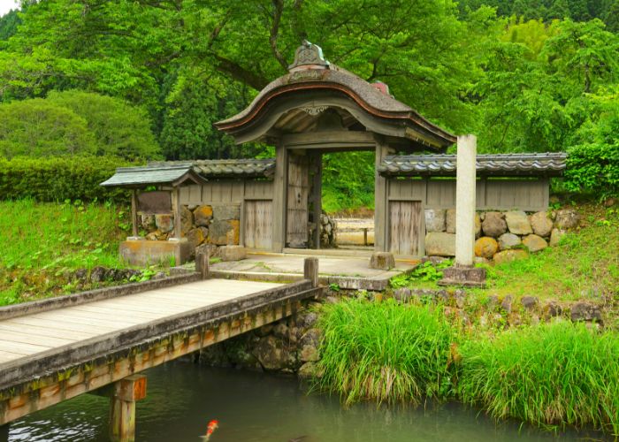A bridge crossing a river, leading to the Ichijodani Asakura Clan Ruins. In the river, a bright koi carp swims.